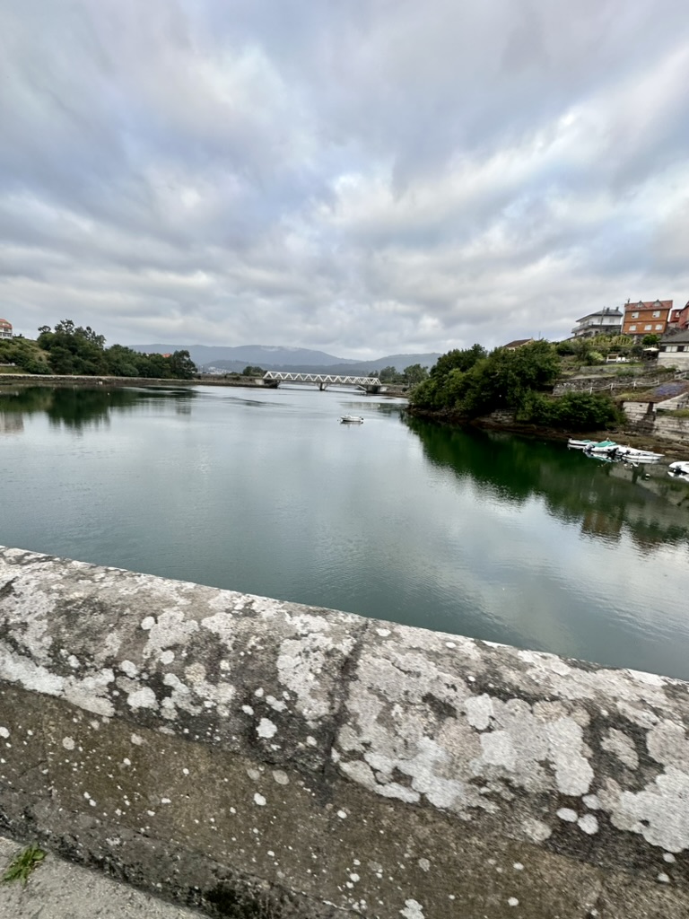 A river, bridge, stone wall, and distant hills along the Camino de Santiago.